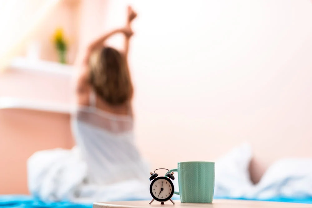 Close-up cup and clock with a stretching woman in the background